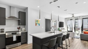 Une cuisine moderne dotée d’un îlot central, d’appareils électroménagers en acier inoxydable et d’une palette de couleurs dans les tons de gris.