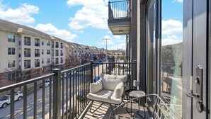 Un balcon doté d’un coin salon avec des coussins, d’une petite table et offrant une vue sur une rangée de maisons de ville.
