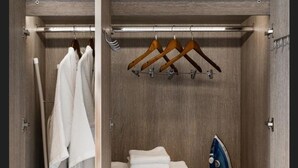 Un vestidor con ropa colgada, toallas dobladas, un plancha y un zapatero.
