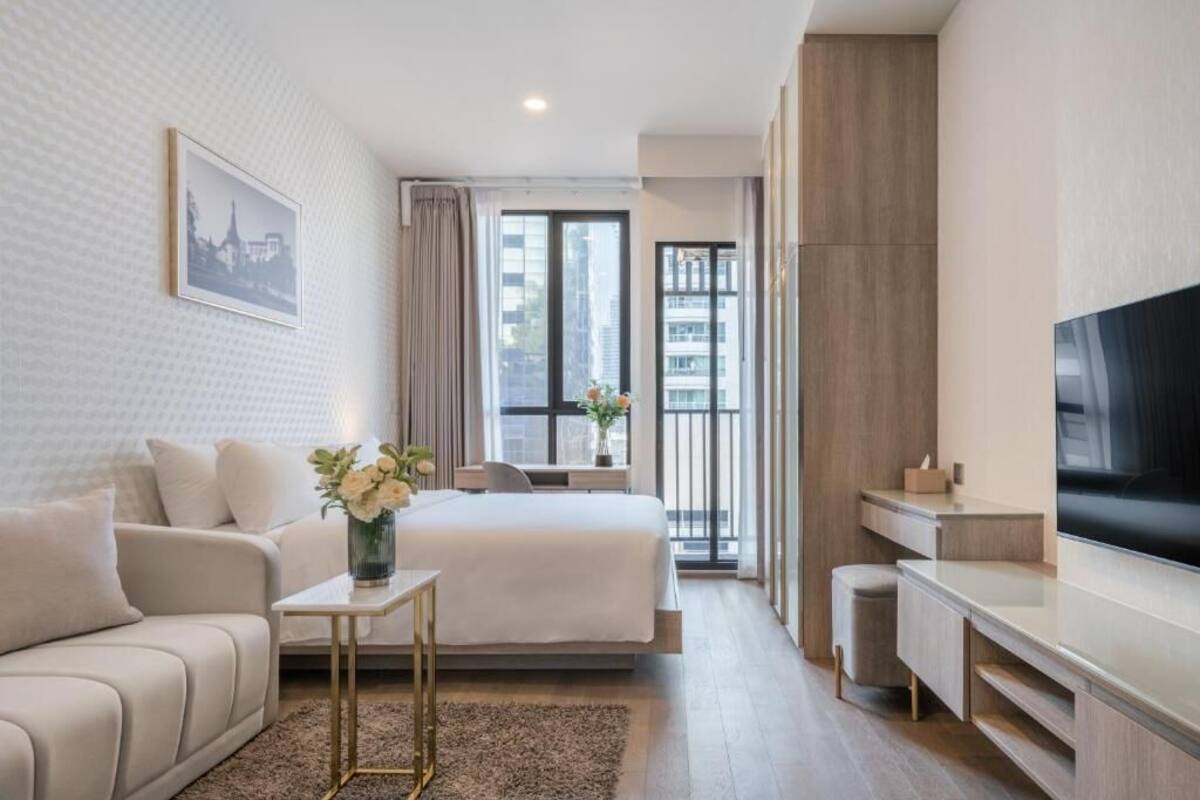 A modern hotel room with a bed, a sofa, a TV, and a desk.