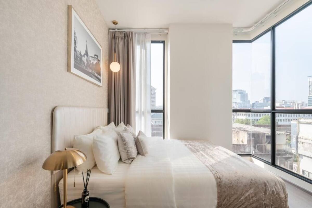 A hotel room with a large window offering a city view, a neatly made bed with white bedding, and a framed picture on the wall.