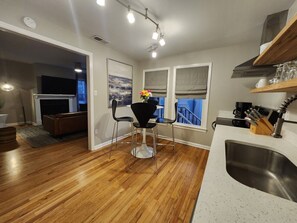 A modern kitchen with a central island, a dining area with chairs, and a view of the outside through large windows. - Forsyth Park Place, Unit C - Sleeps 4, Three Minute Walk to Forsyth Park (Savannah)
