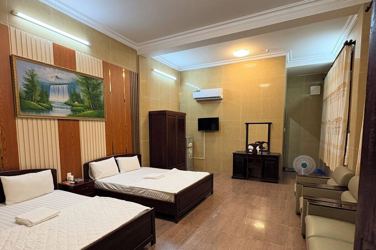 Een hotelkamer met twee bedden, een televisie, een airconditioner, een schilderij, een kledingkast en een badkamer met douche en ventilator.