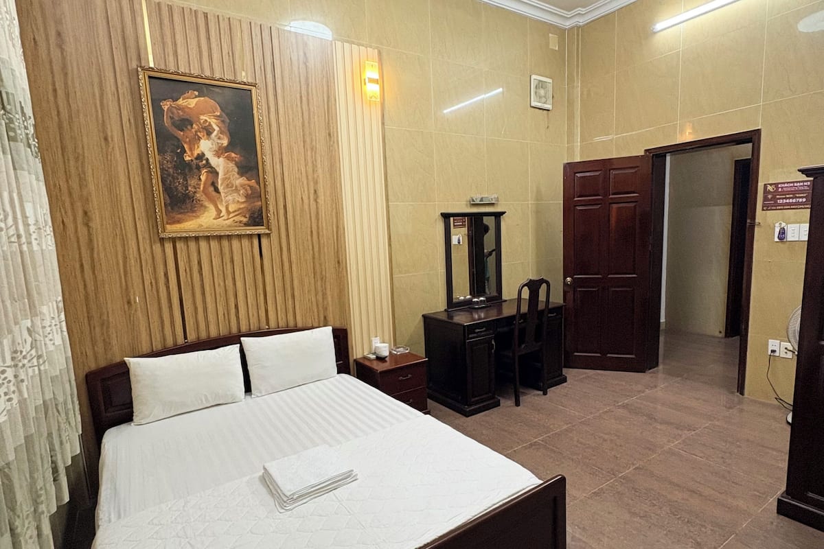 Een hotelkamer met een groot bed, een houten hoofdeinde, een schilderij aan de muur, een bureau met stoel en een kledingkast.