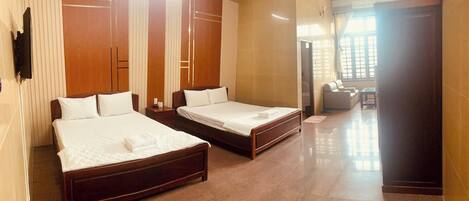A hotel room with two wooden beds, a TV, and a sofa in the adjacent living area.