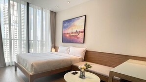Una habitación de hotel con una cama, un sofá, una mesa redonda de vidrio y un cuadro de un paisaje urbano.