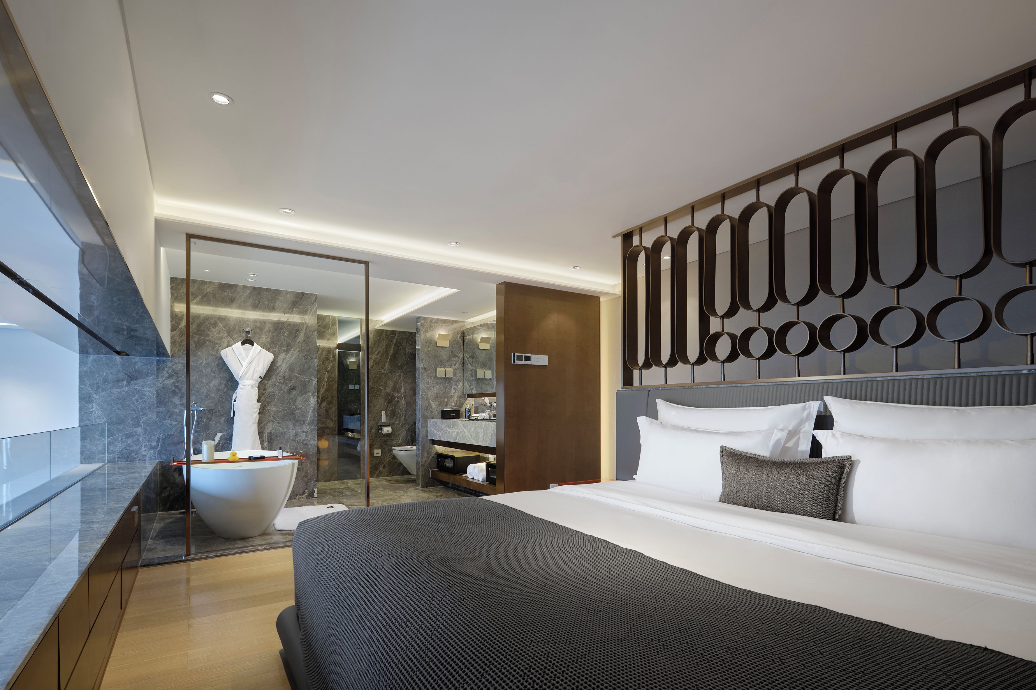 A modern hotel room with a large bed, a bathtub, a glass shower enclosure, and a marble-tiled bathroom.
