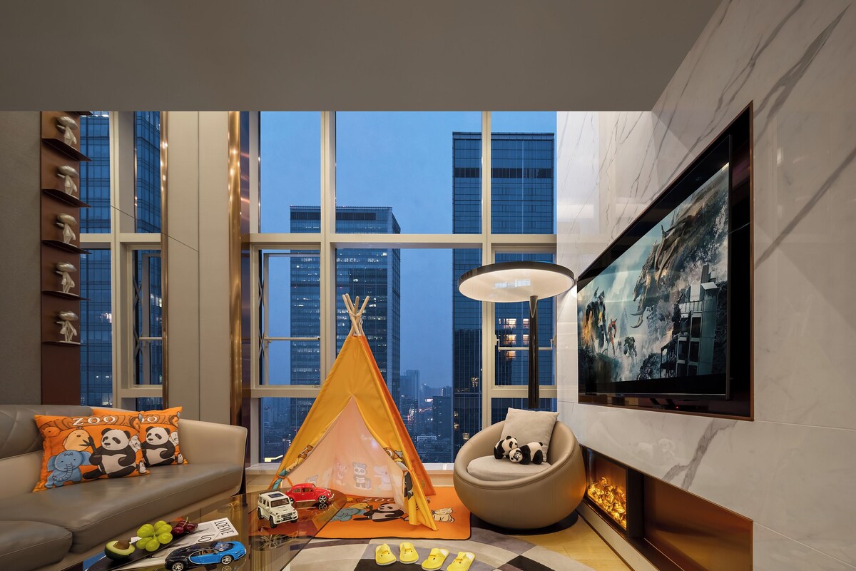 Una sala de estar moderna con un ventanal grande, un sofá con almohadones de estilo panda, una carpa infantil, un sillón redondo y un televisor de pantalla plana.