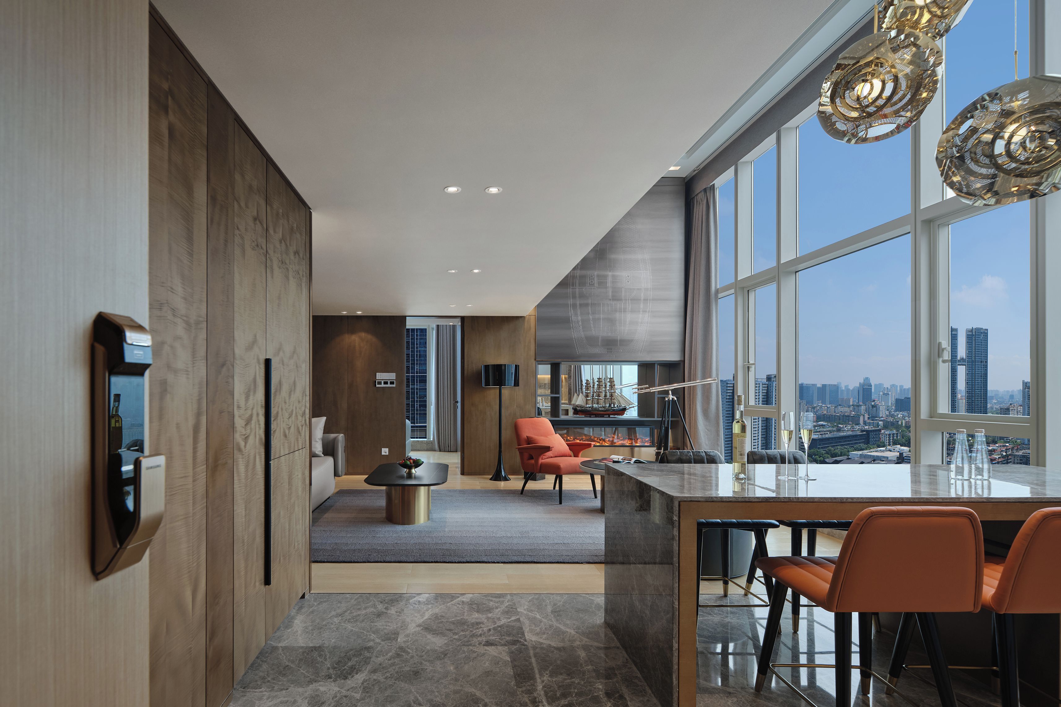 A modern kitchen with a large island, a dining area with orange chairs, and a view of the city through large windows.