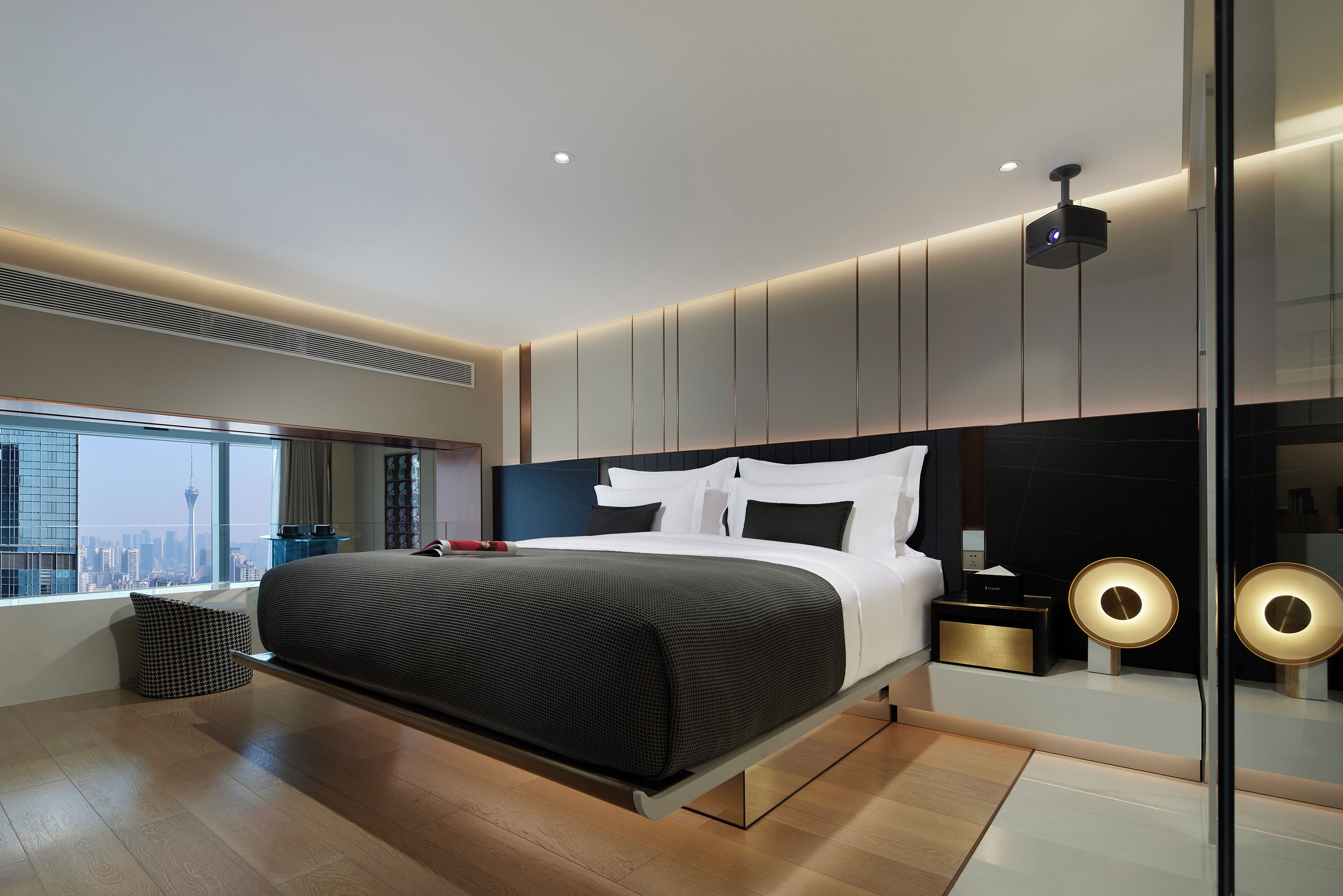 A modern bedroom with a large bed, a city view, and a unique ceiling projector.
