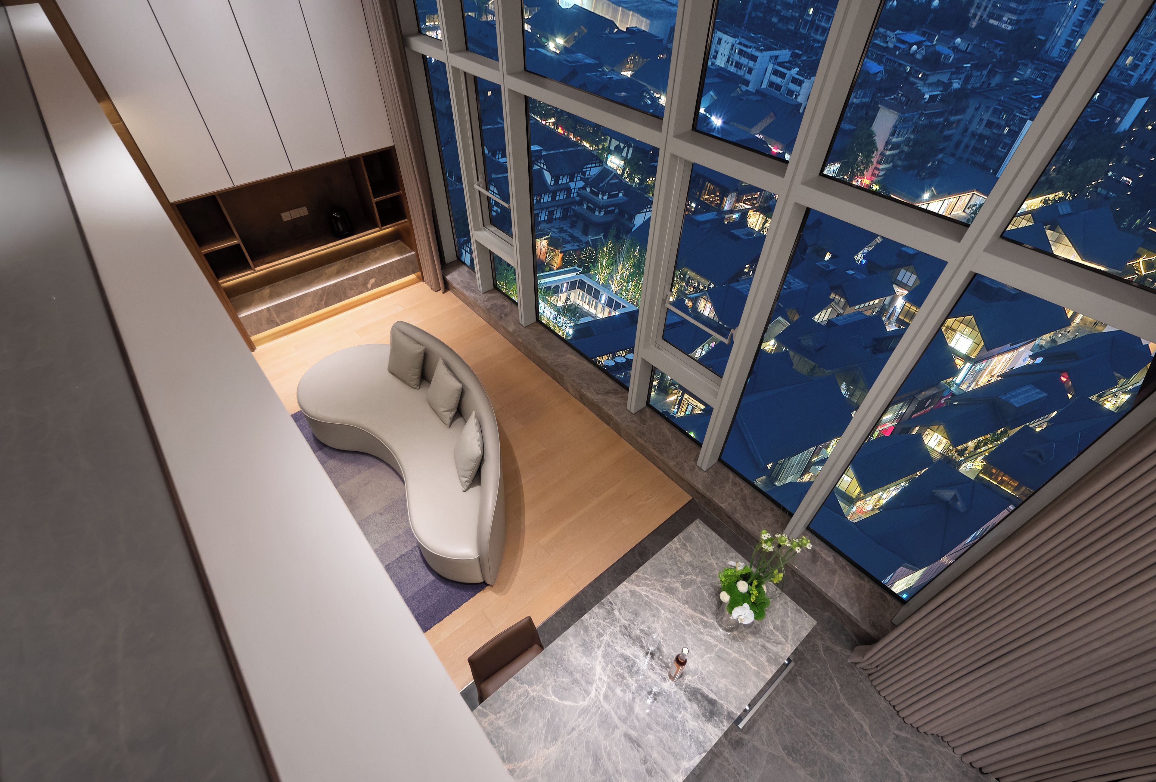 Ein modernes Wohnzimmer mit einer gebogenen Couch, einem kleinen Tisch und einem großen Fenster mit Blick auf die Stadt.
