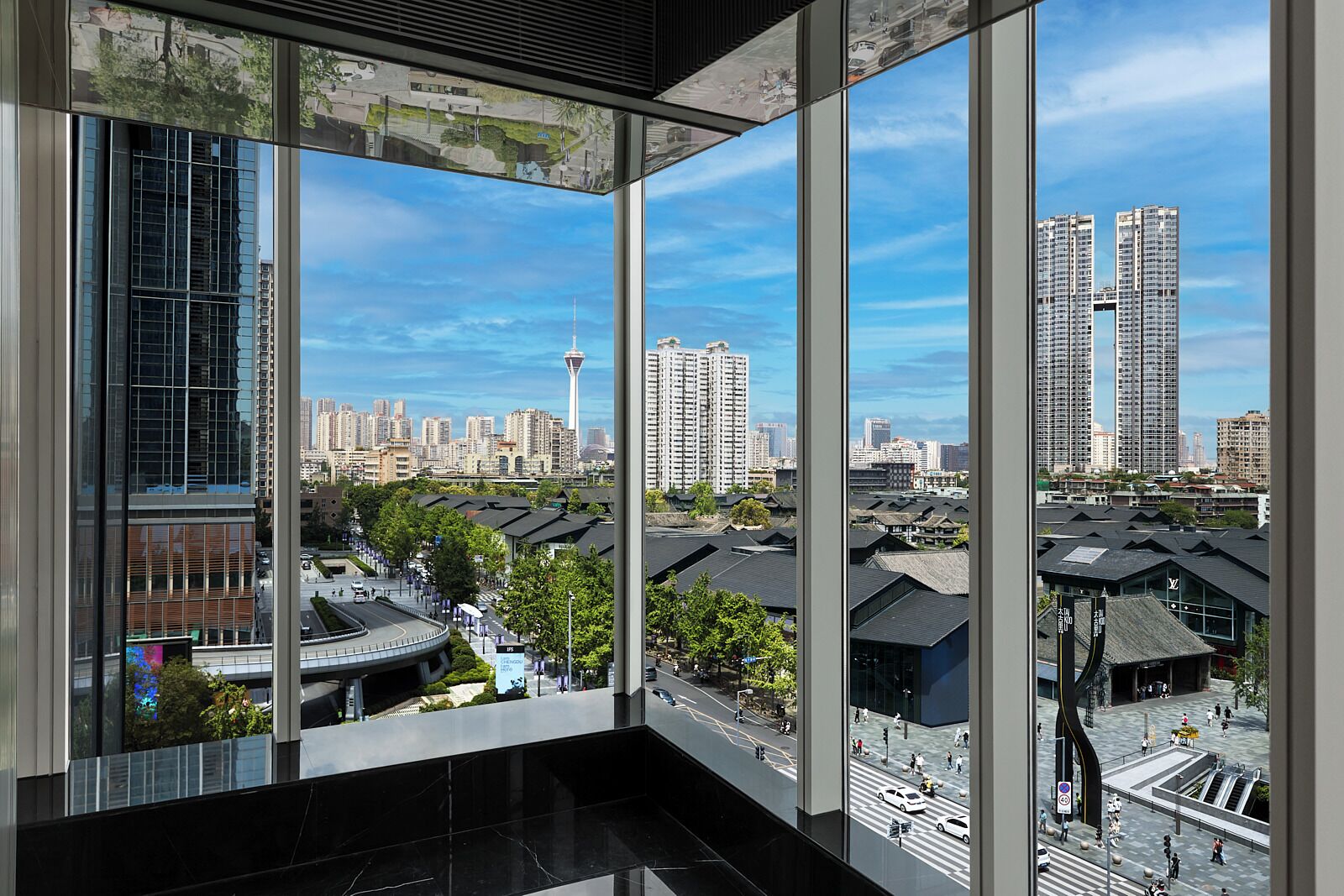 A modern building with large windows offering views of a cityscape, including high-rise buildings and a tower.