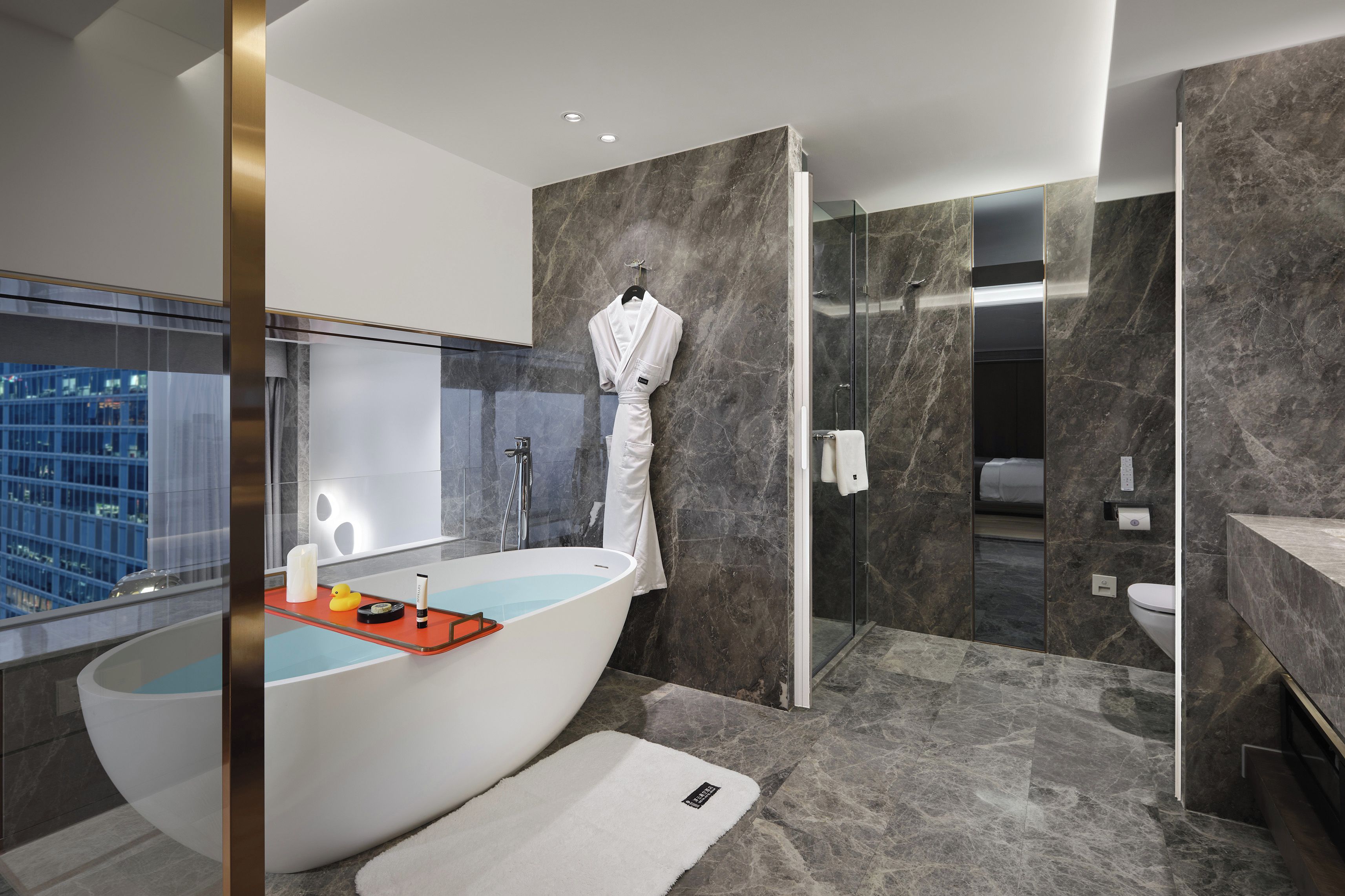 Un baño moderno con una bañera independiente, una ducha con mampara de vidrio y vistas a la ciudad.