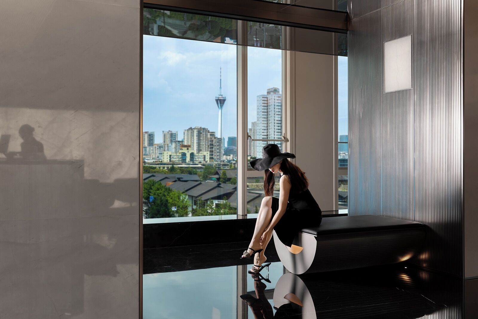 A modern interior with a large window offering a city view, a reflective floor, and a seating area.