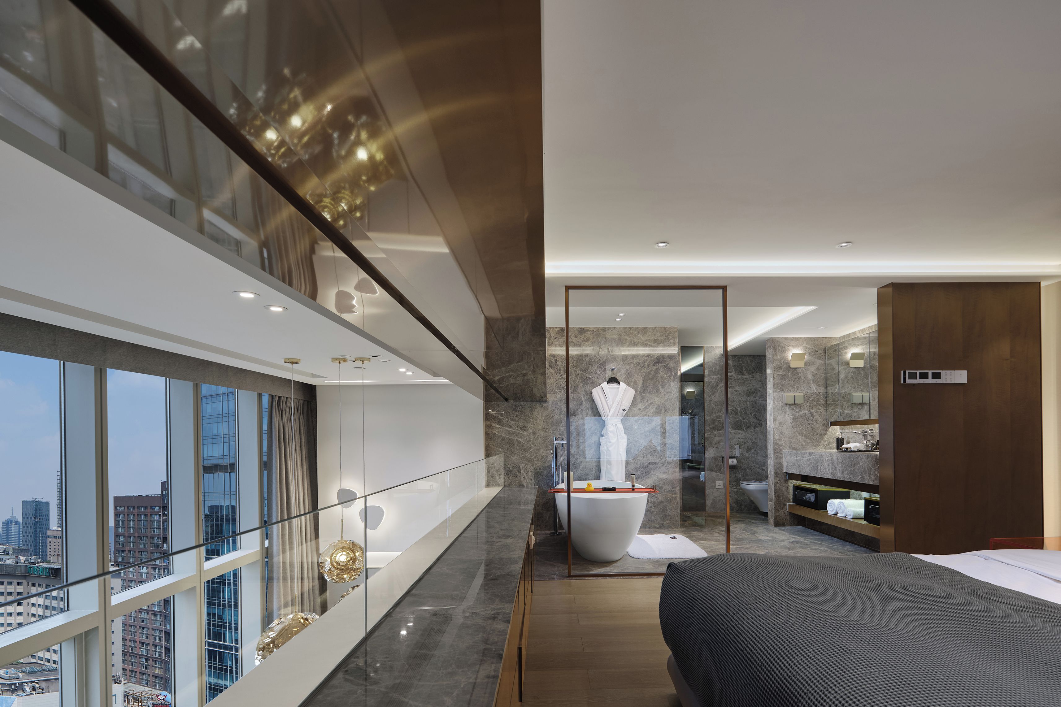 A modern hotel room with a large bed, a glass-enclosed balcony, a marble bathroom, and a city view.