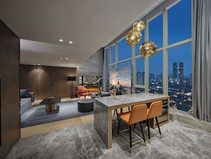 A modern living room with a large window, a dining area, and a view of the cityscape at dusk.