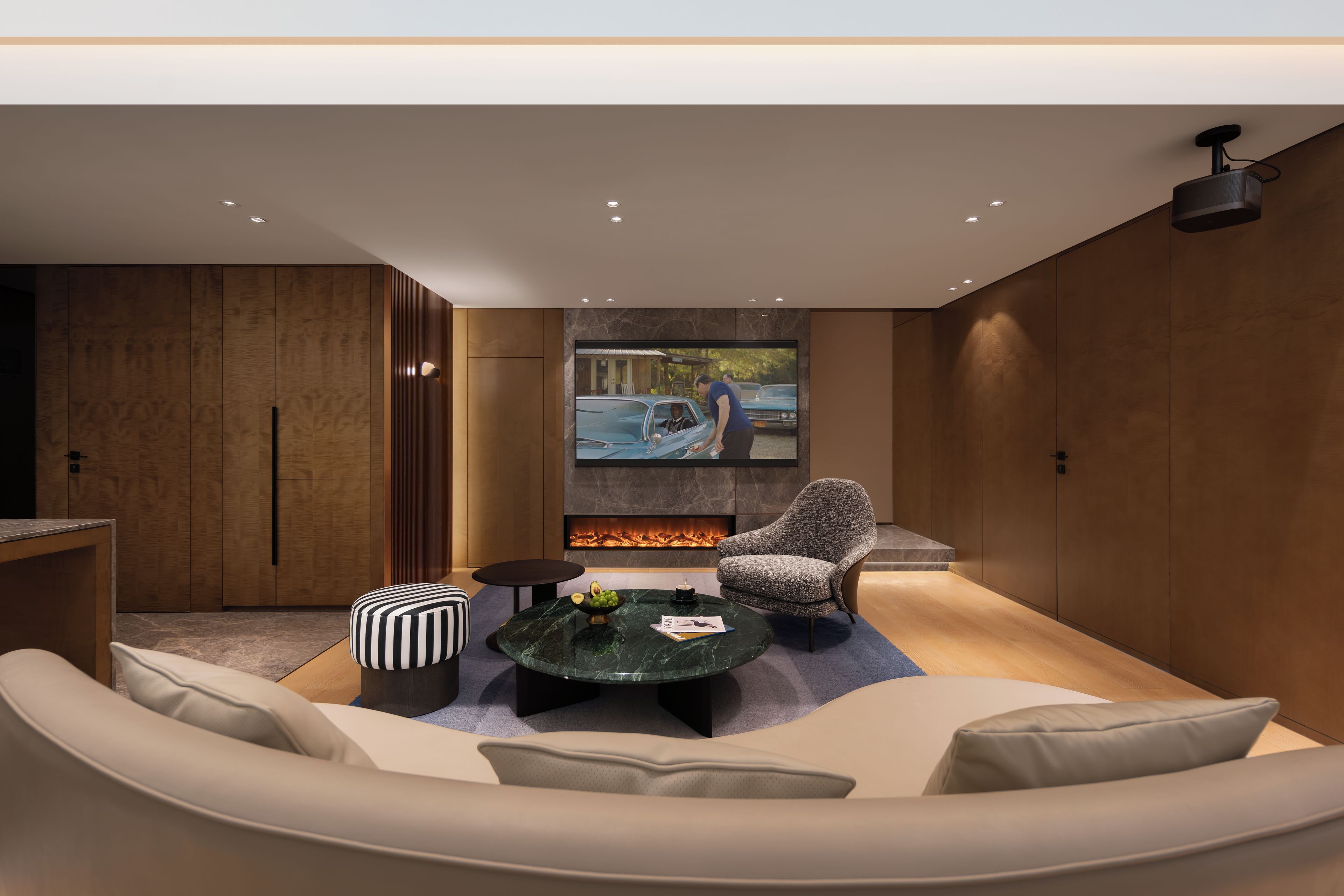 A modern living room with a sofa, a round coffee table, a fireplace, and a television screen displaying a scene.