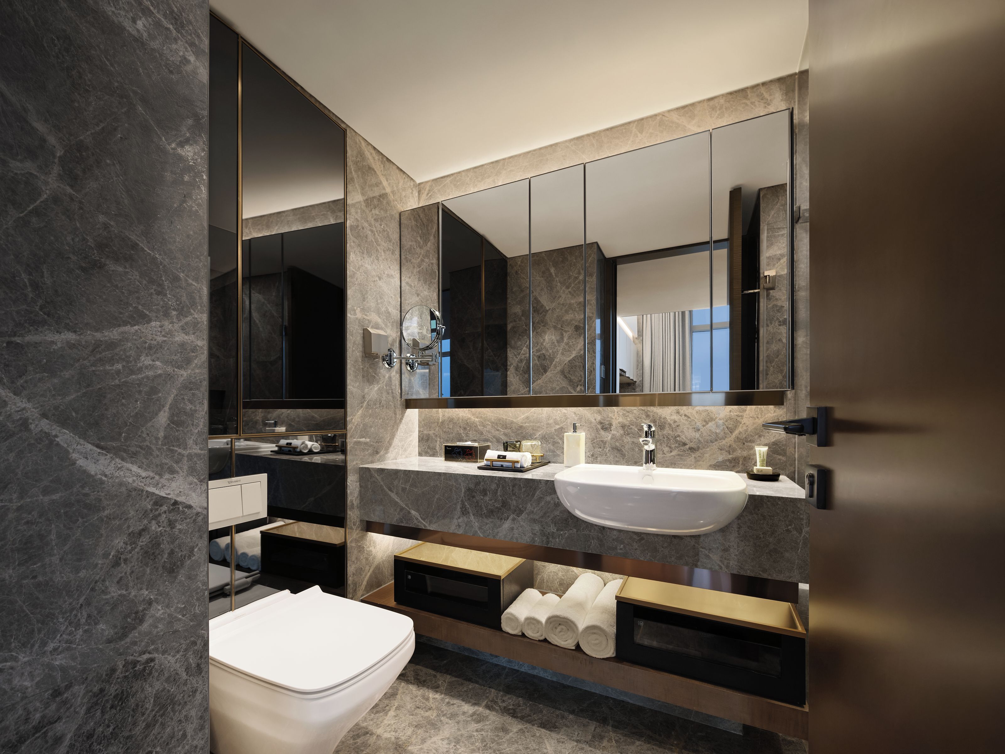 A modern bathroom with a marble sink, a large mirror, and a toilet.