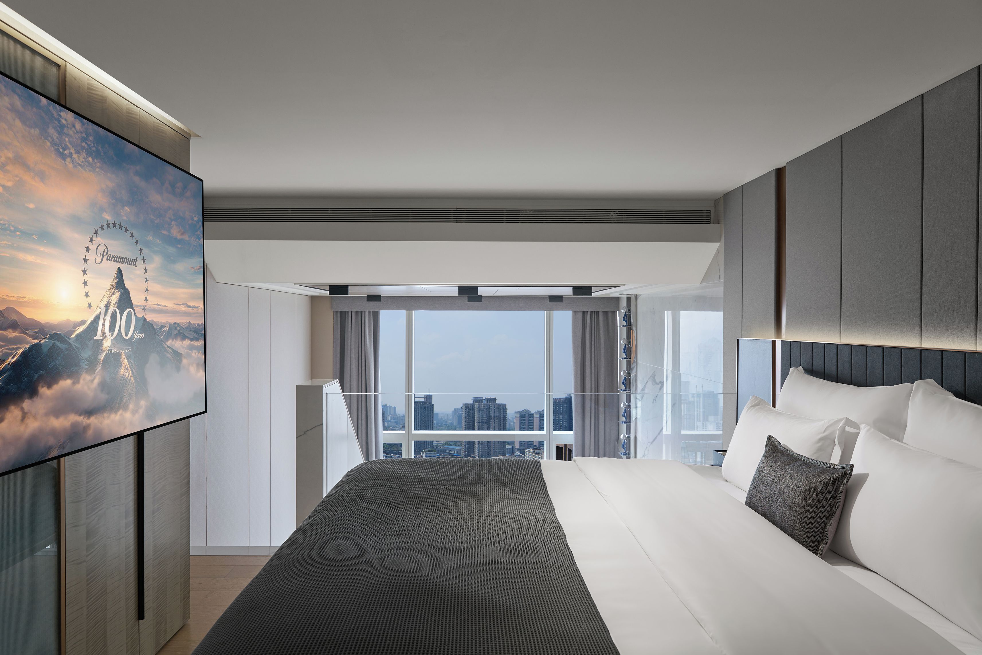 Una habitación de hotel moderna con una cama grande, vistas a la ciudad y un ventanal panorámico.