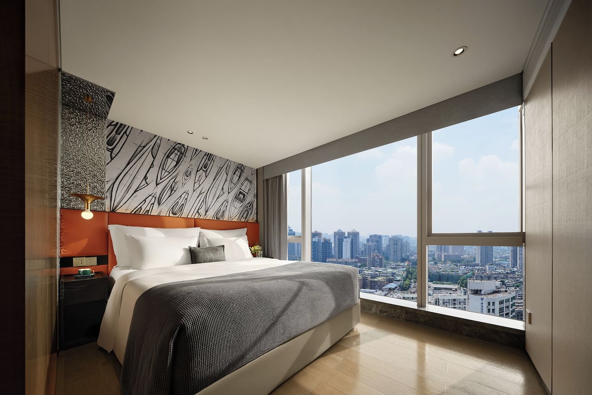 Una moderna camera d'albergo con un ampio letto, vista sulla città e una testiera a motivi decorativi.