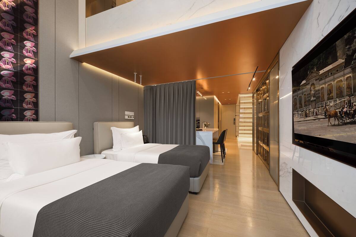 Una camera d'albergo moderna con un letto grande, una scrivania e una televisione che mostra una vista sulla città.