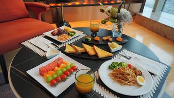 A dining table with a variety of food items, including fruits, vegetables, and a hot beverage, set against a backdrop of a fireplace.
