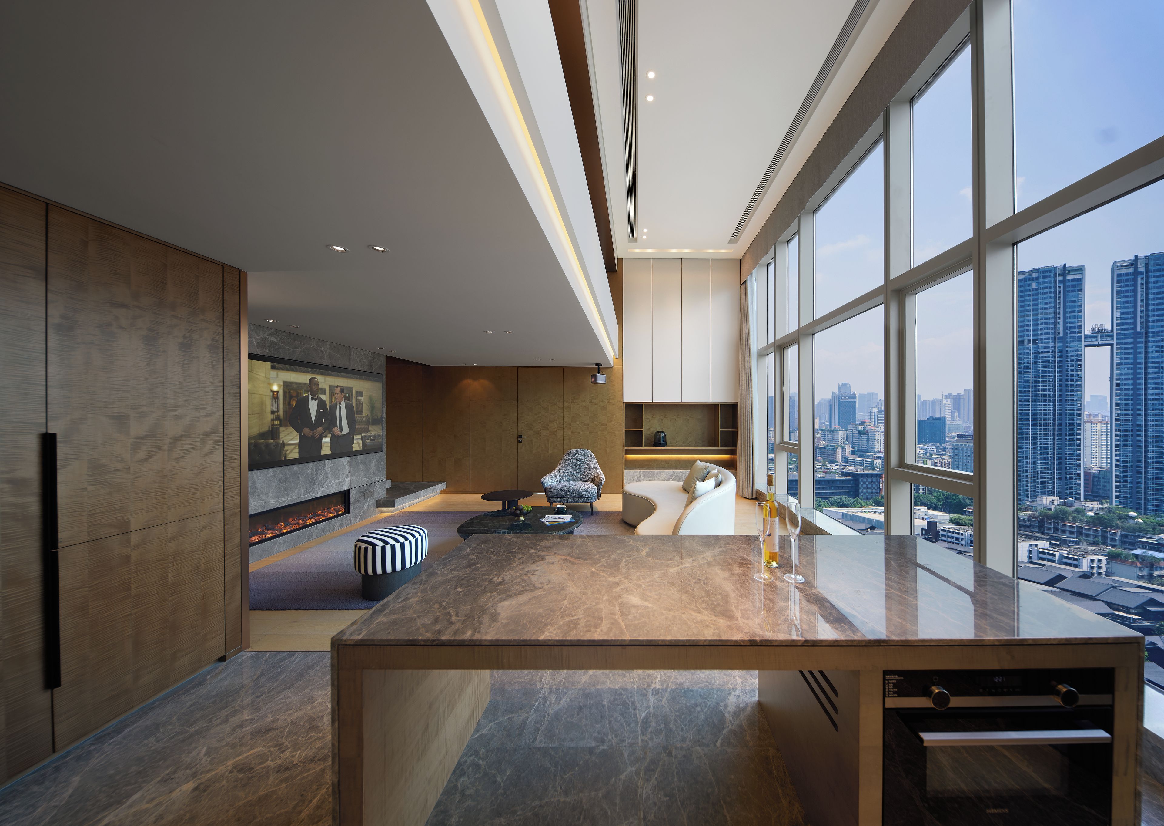 A modern kitchen with a large island, a built-in fireplace, and a city view through large windows.