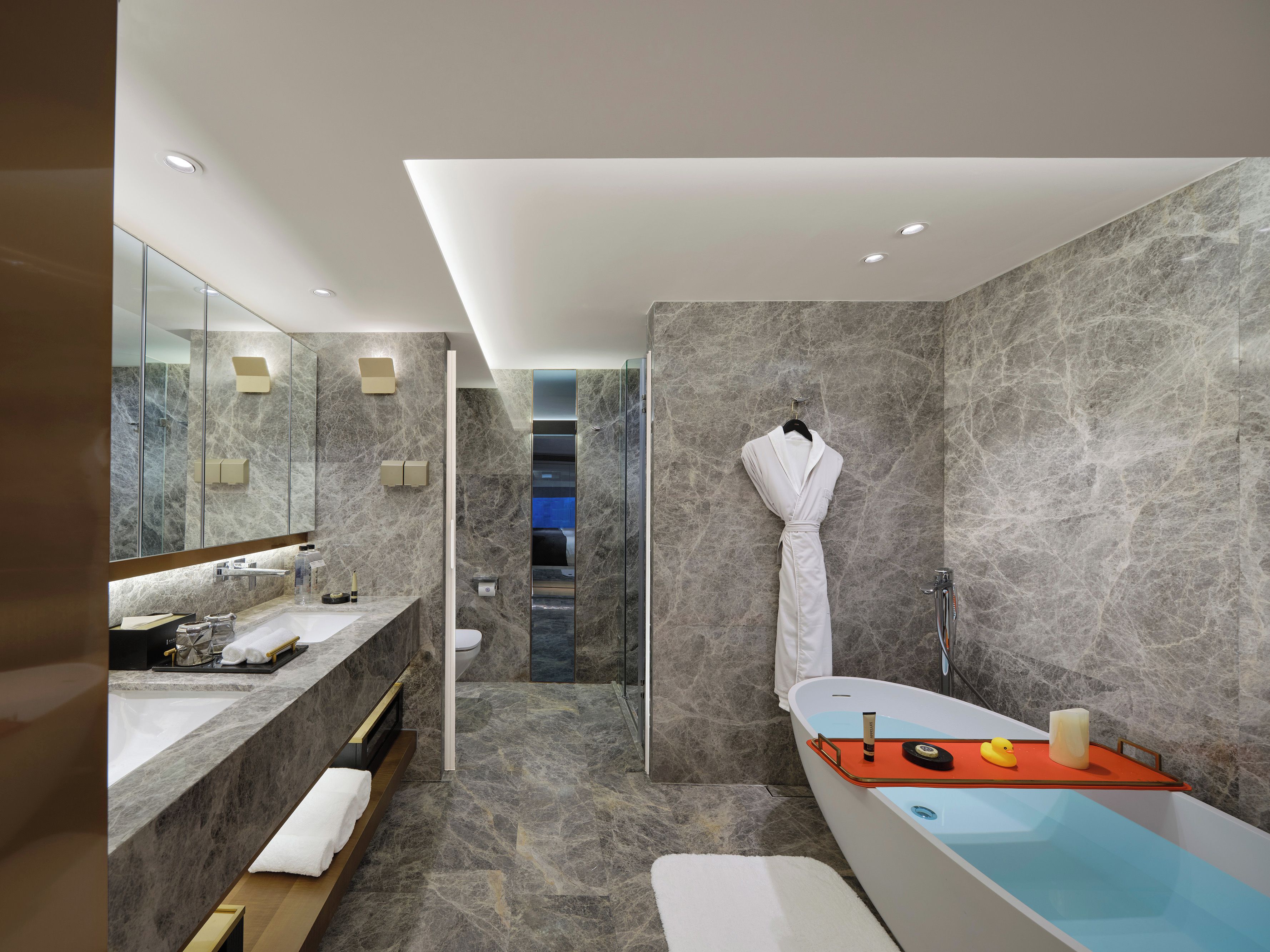A modern bathroom with a marble wall, a large mirror, a bathtub, and a shower area.