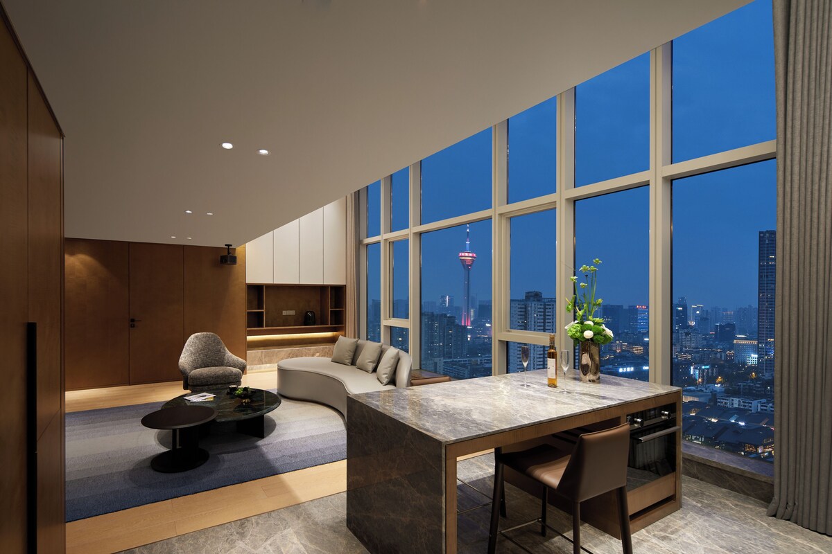 Una sala de estar moderna con un sofá curvo, un comedor con una mesa de mármol y ventanas amplias que ofrecen vistas a la ciudad.