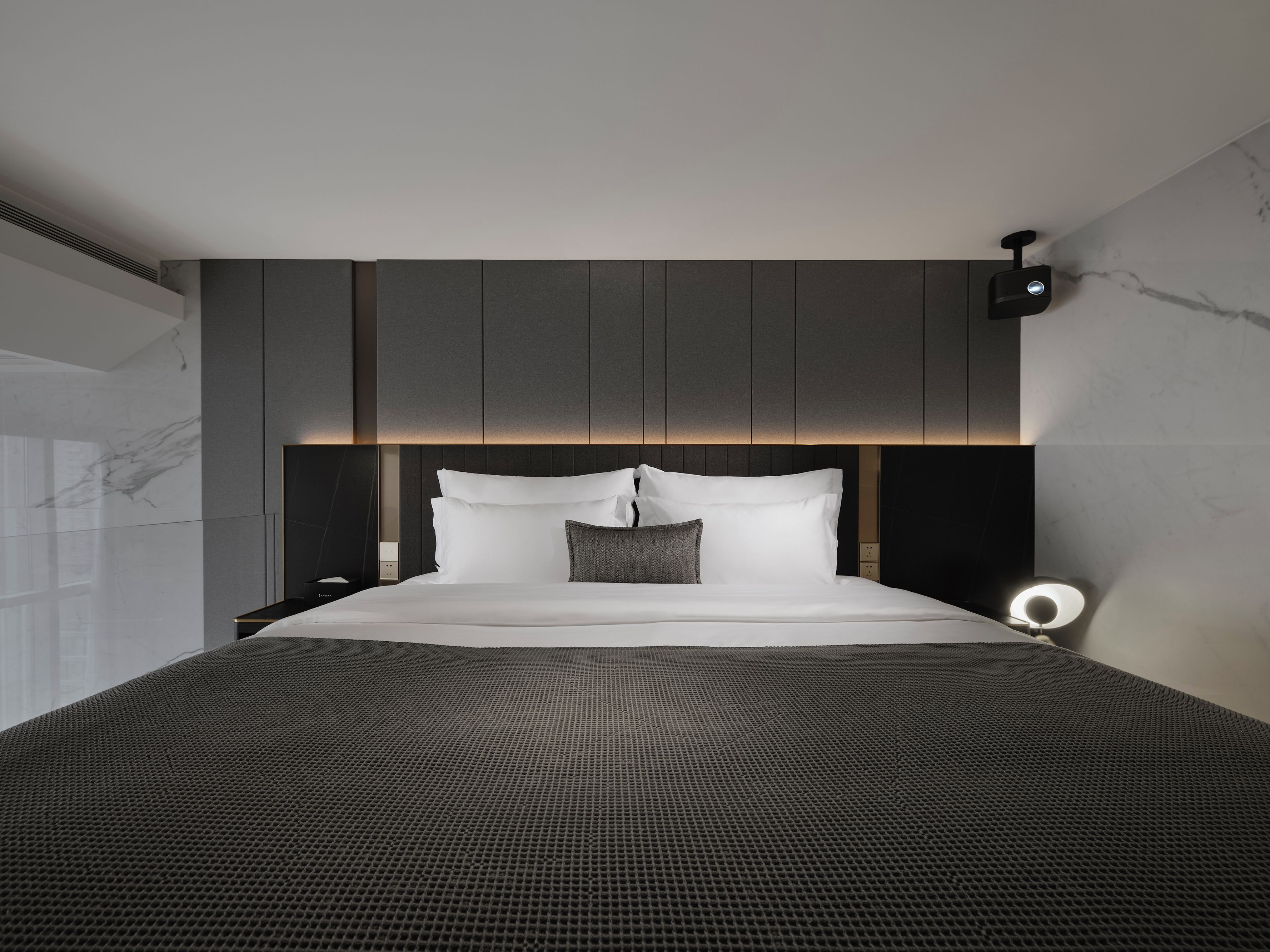Una camera da letto moderna con un letto grande, una testiera con illuminazione integrata, un comodino e una lampada a parete.