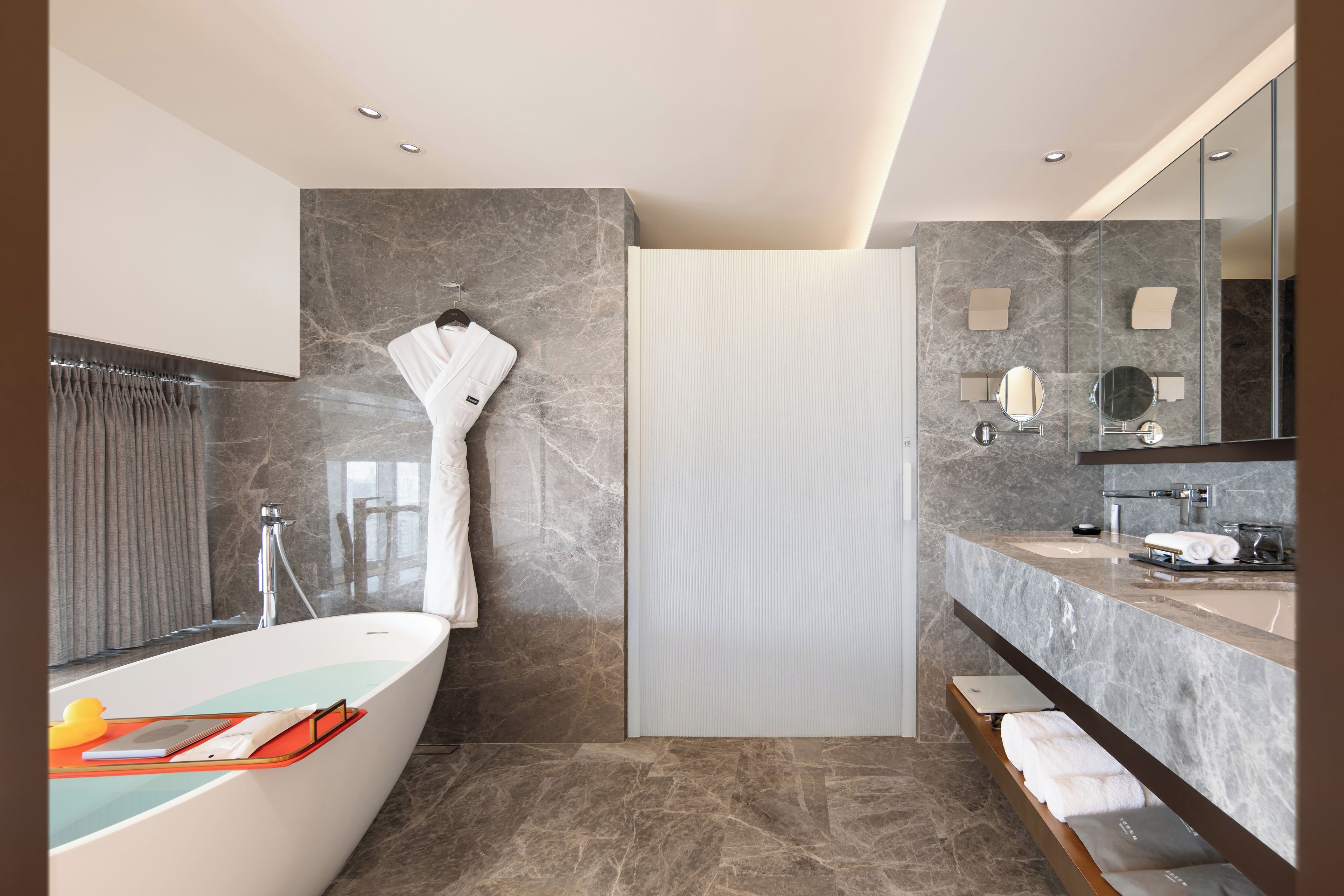 A modern bathroom with a freestanding bathtub, a large mirror, and a vanity with a sink and towel rack.