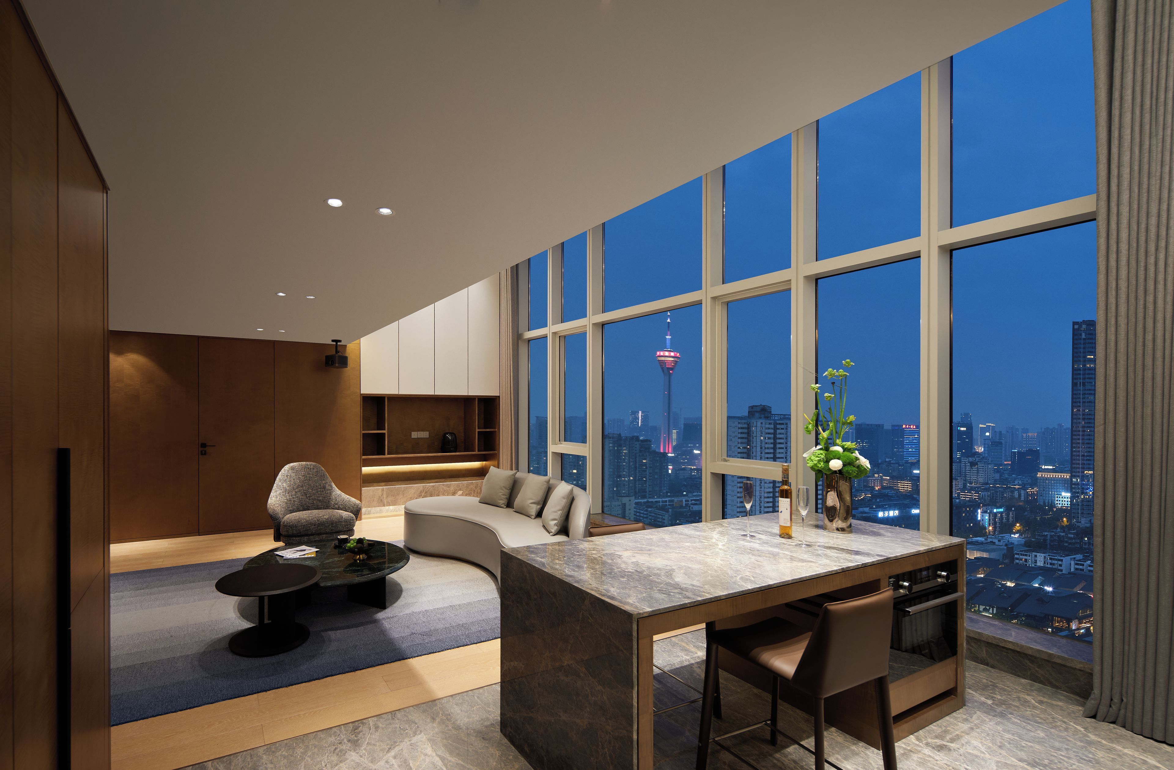 A modern living room with a curved sofa, a dining area with a marble table, and large windows offering a city view.