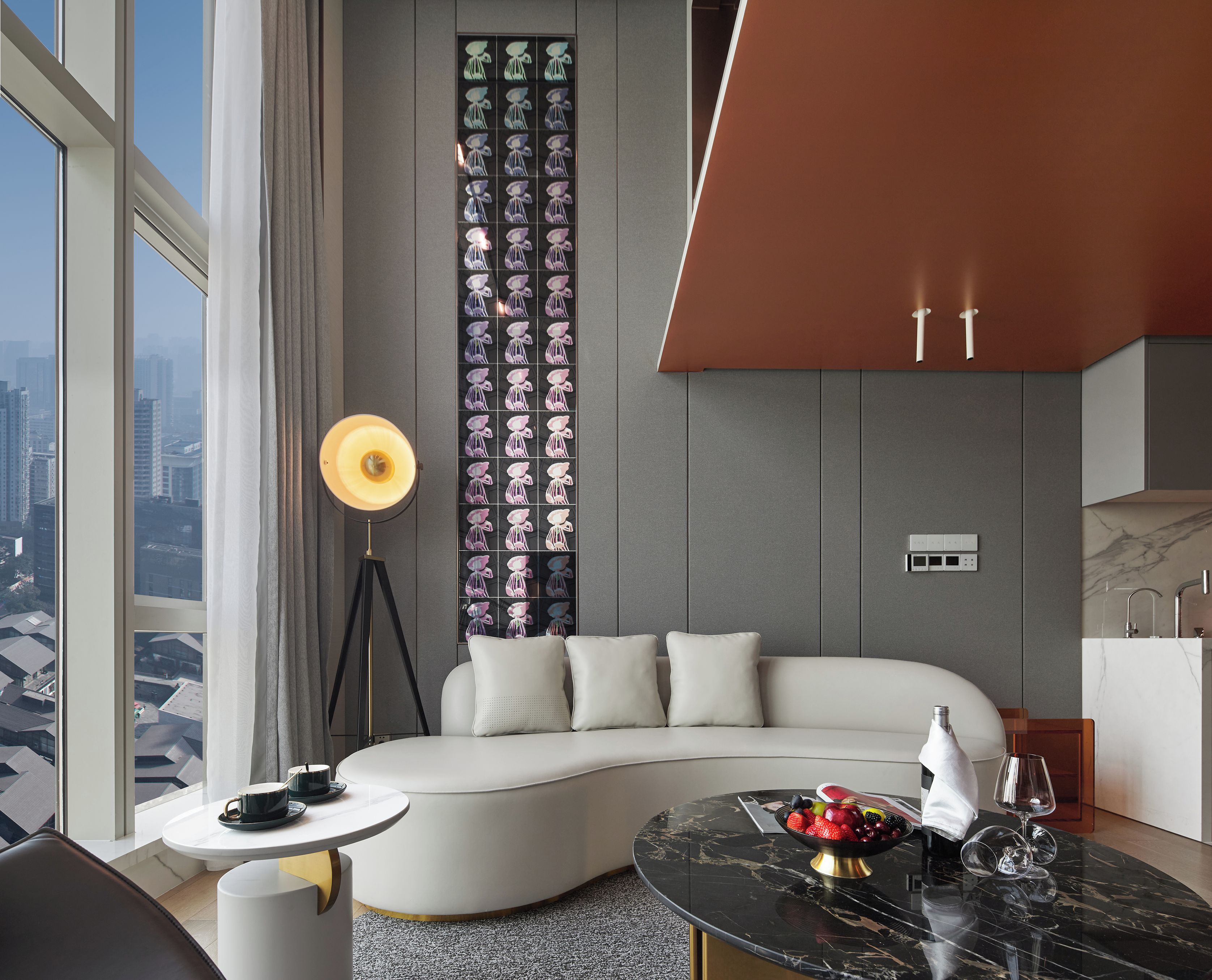 A modern living room with a curved sofa, a round coffee table with fruit, a floor lamp, and a city view through large windows.