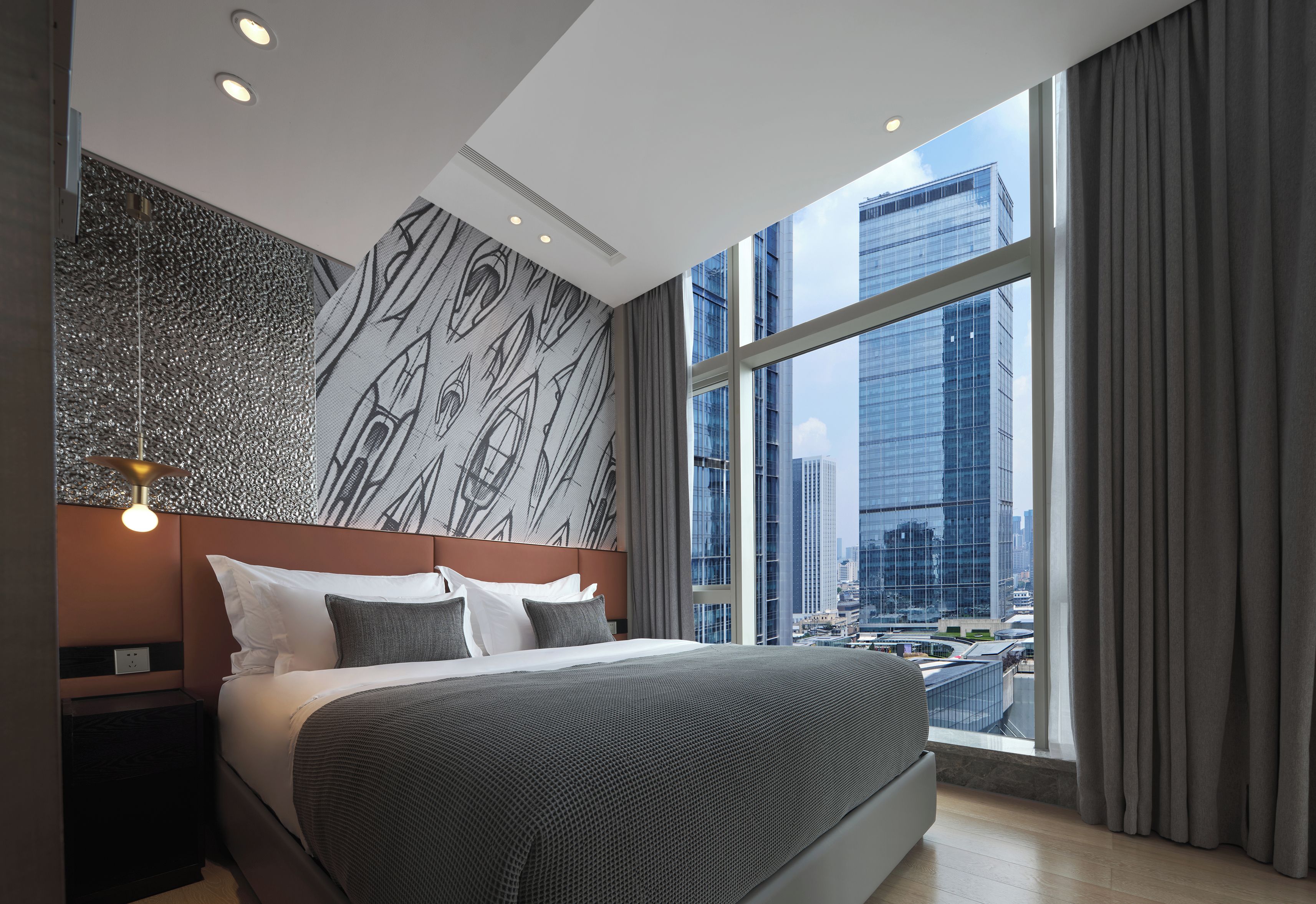 A modern hotel room with a large bed, a city view, and a patterned wall.