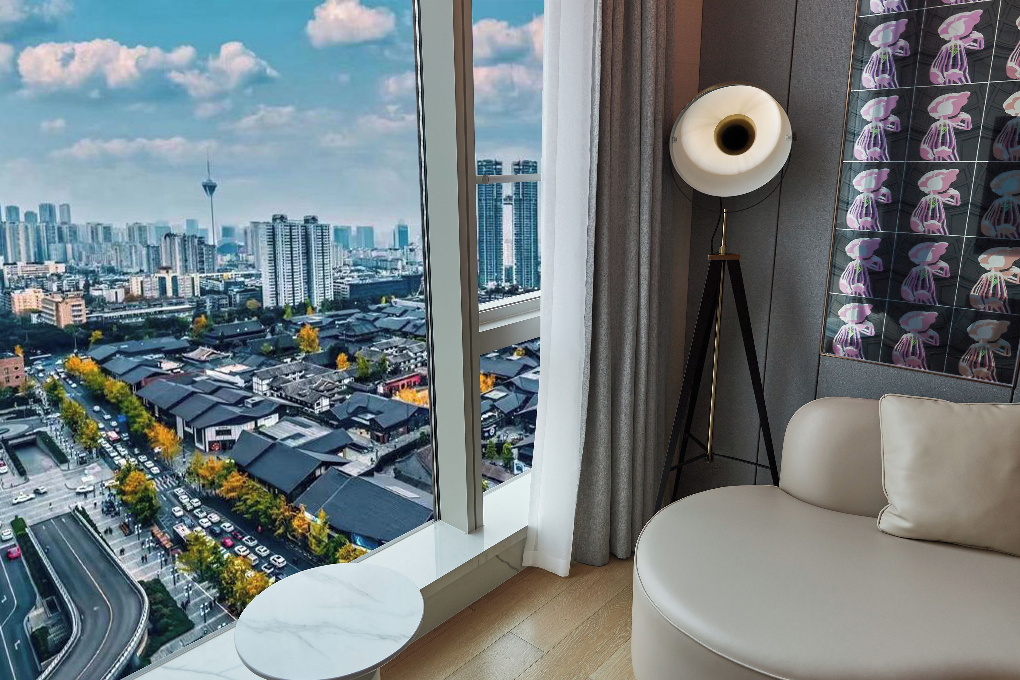 Una sala de estar moderna con un ventanal que ofrece vistas a la ciudad, una mesa redonda, un sofá y una lámpara de pie.
