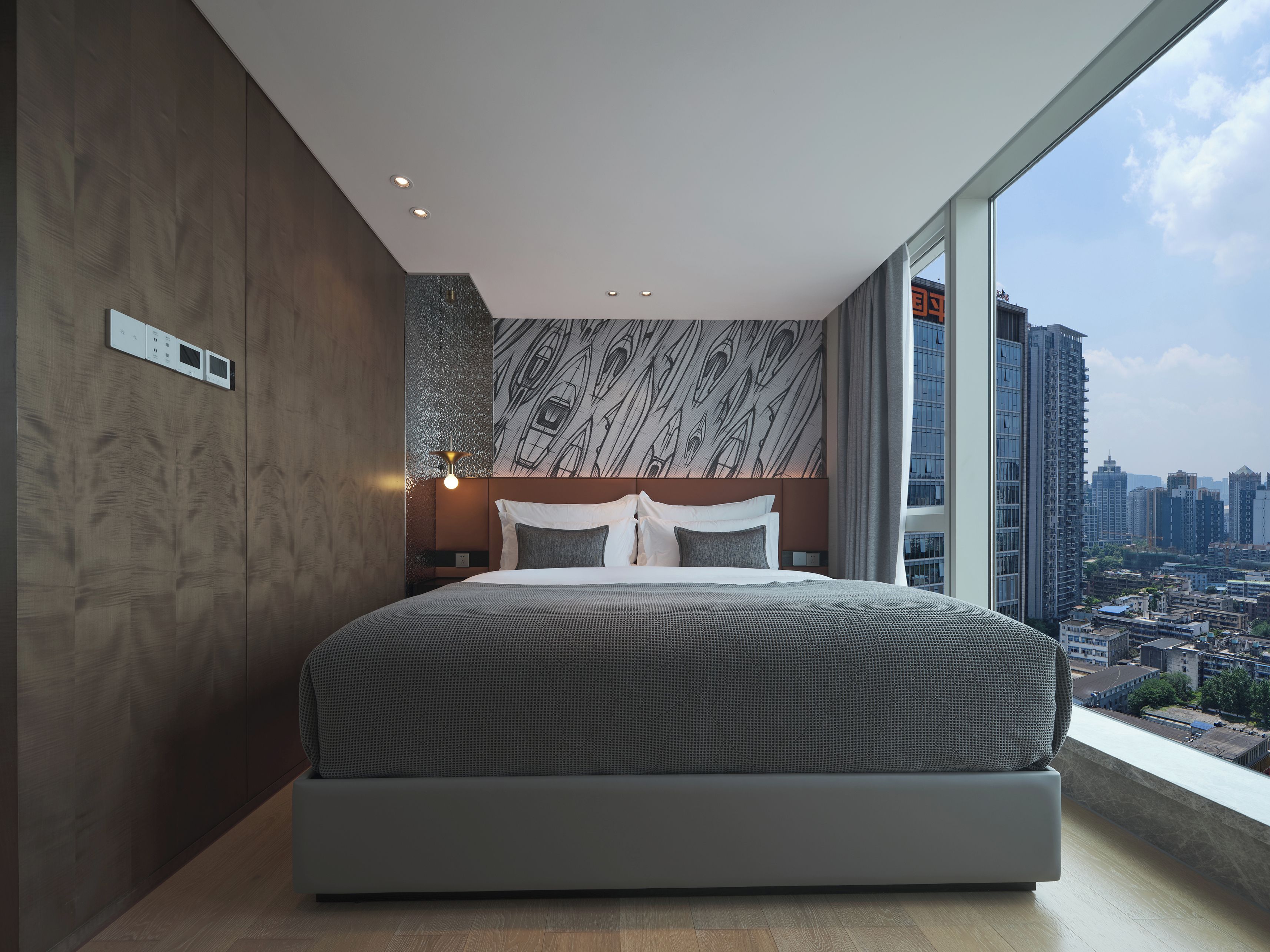 Une chambre moderne avec un grand lit, une vue sur la ville et un mur décoré de motifs.