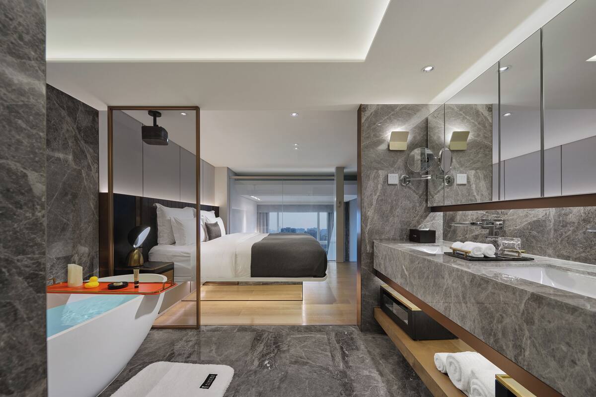 Una camera d'hotel moderna con un letto grande, un bagno con un piano di lavoro in marmo e vista sulla città.