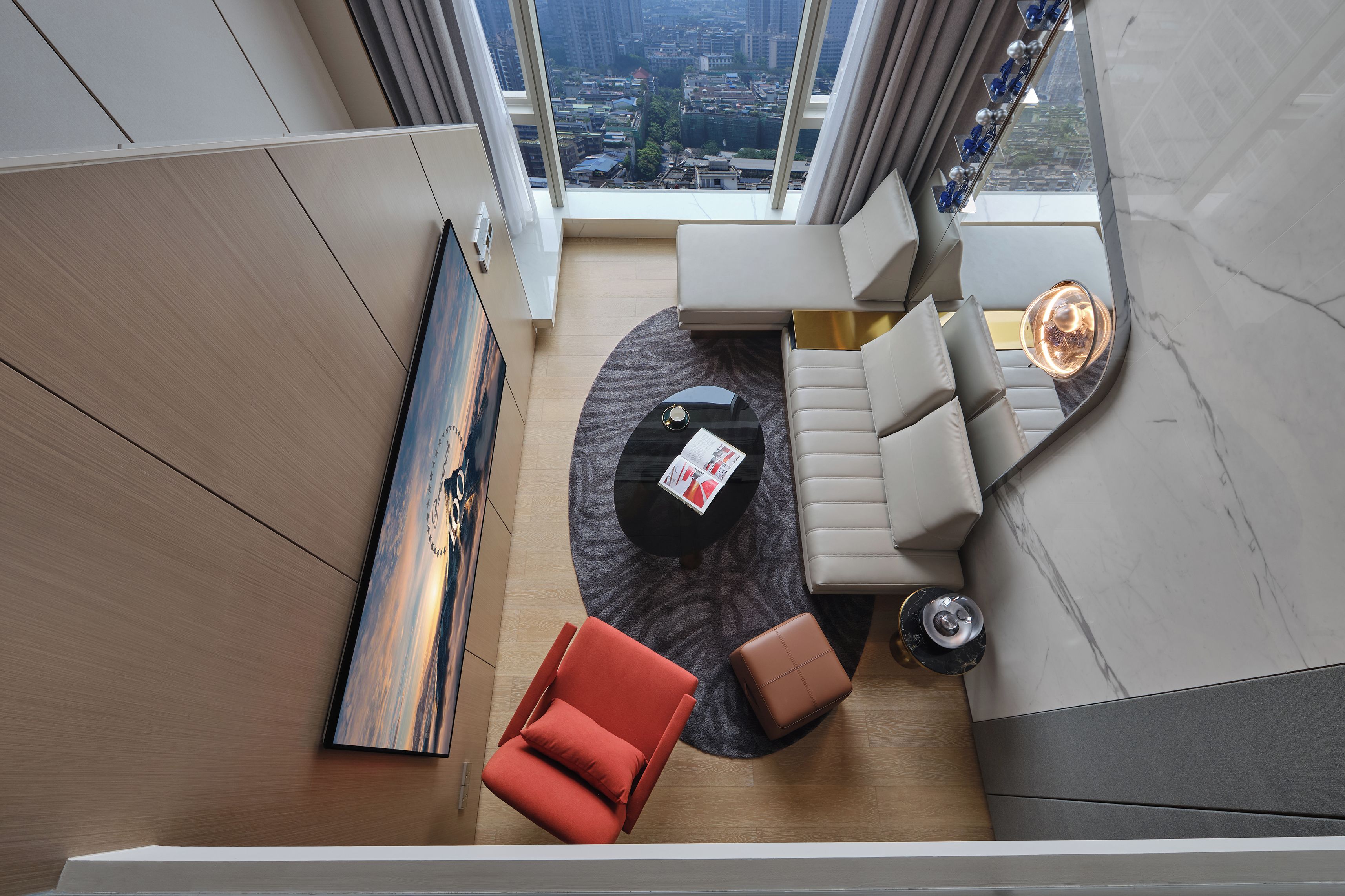 A modern living room with a sofa, a red chair, a coffee table, and a view of the city through large windows.