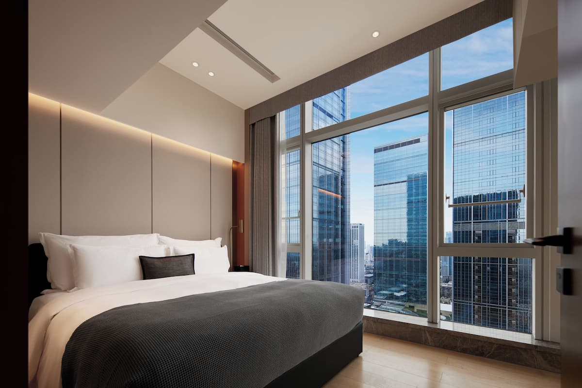 Una camera d'albergo moderna con un letto grande, vista sulla città e un'ampia finestra.