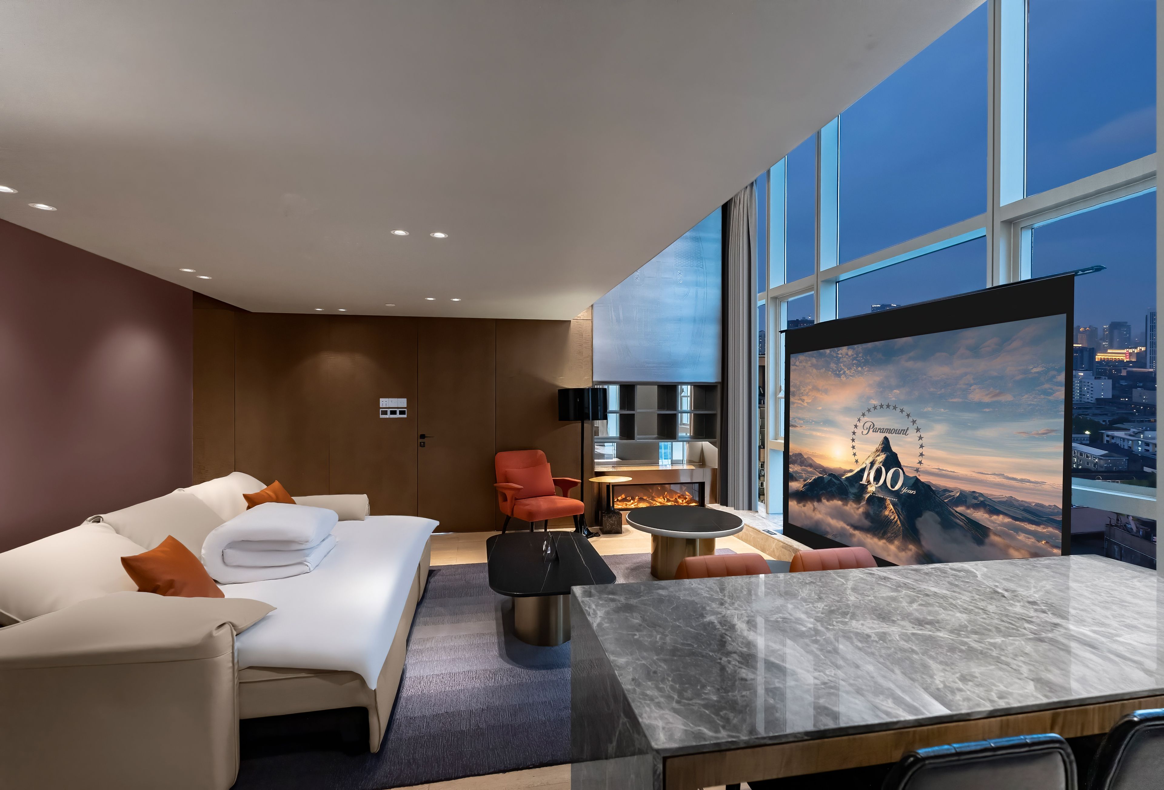 A modern hotel room with a large bed, a seating area with a coffee table, and a TV displaying a mountain view.