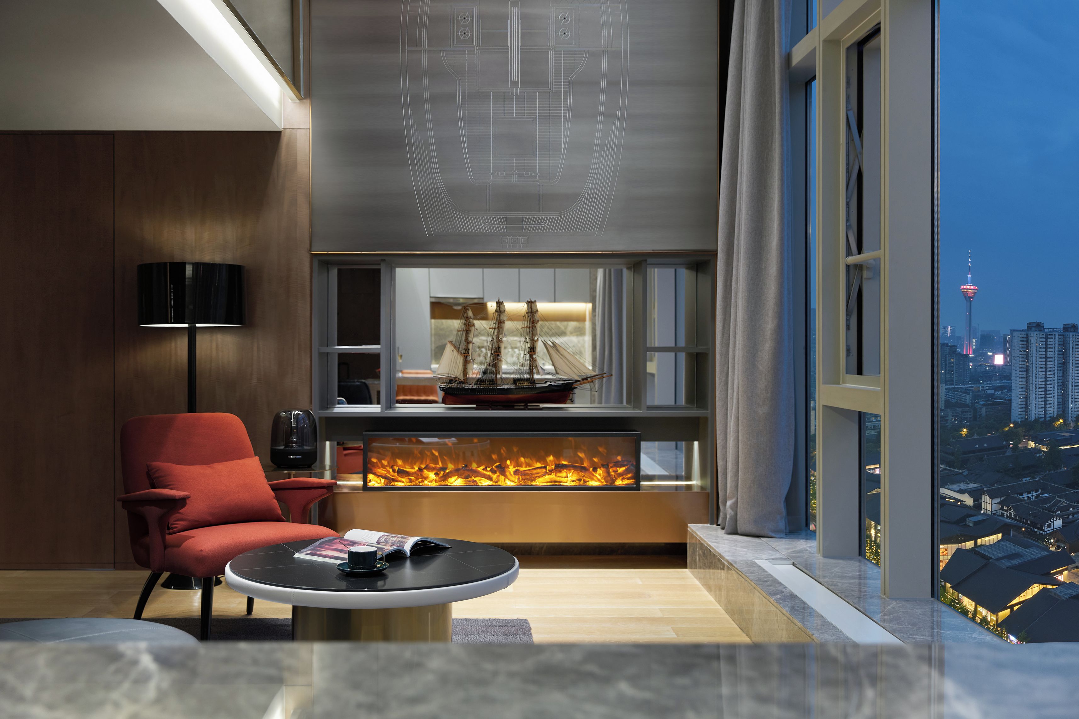 A modern living room with a red armchair, a round coffee table, a ship model, and a fireplace.