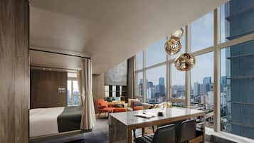 A modern hotel room with a large bed, a dining area, and a city view through large windows.