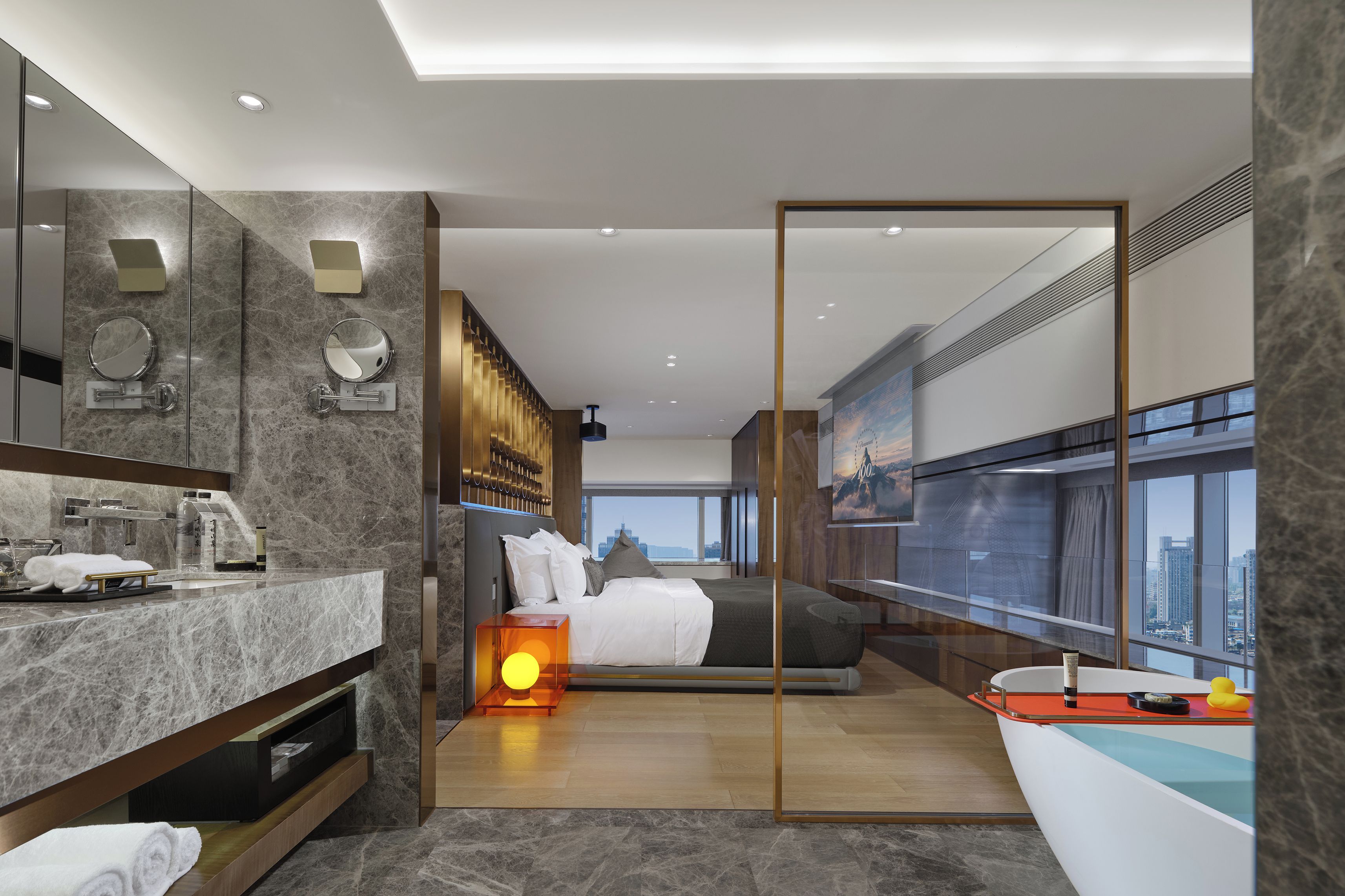 A modern hotel room with a large bed, a bathroom with a marble vanity, and a city view through large windows.