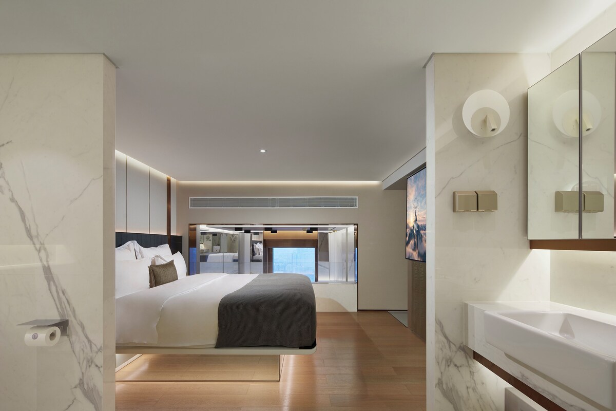 Una habitación de hotel moderna con una cama grande, un armario empotrado, un espejo amplio y un baño independiente.