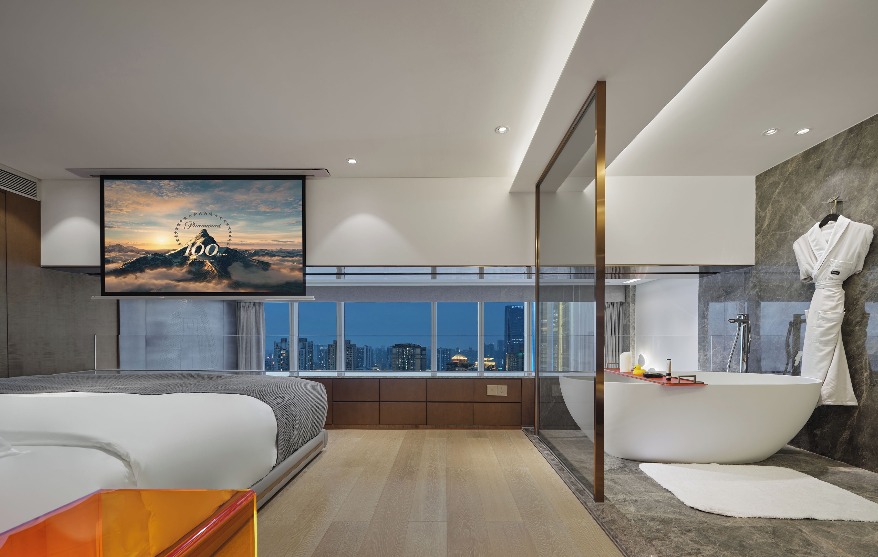 A modern bedroom with a large bed, a bathtub, and a city view.