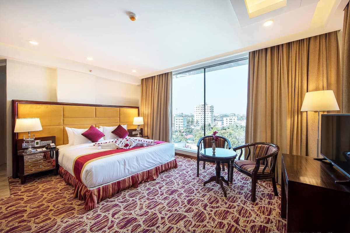 Quarto de hotel com uma cama grande, uma escrivaninha, uma cadeira e uma televisão.