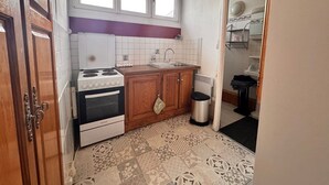 Une cuisine compacte équipée d’une cuisinière, d’un four et d’un évier, de placards en bois, d’une fenêtre au-dessus de l’évier et de carreaux de sol à motifs.