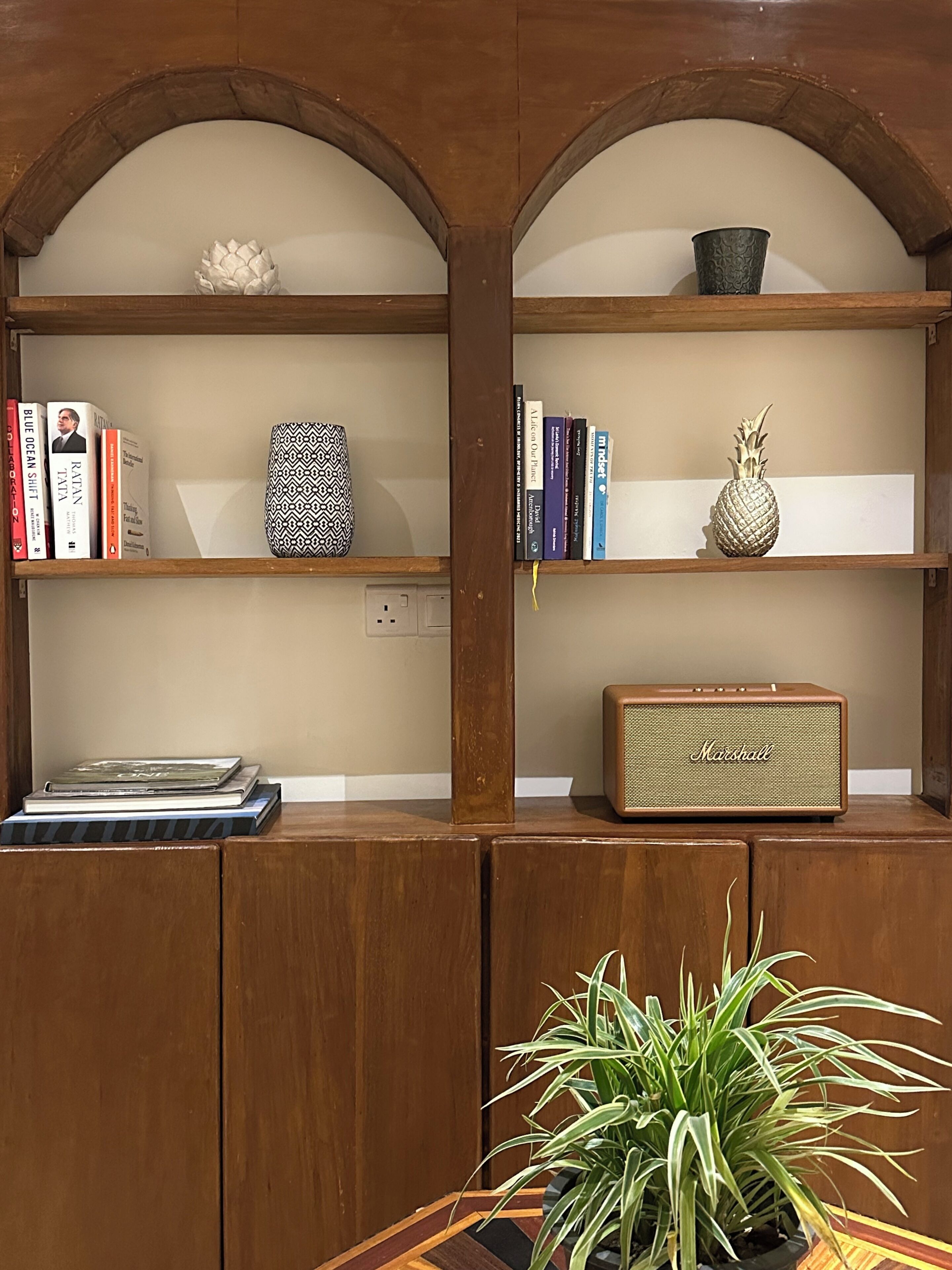 A wooden bookshelf with books, a decorative pineapple, a patterned vase, and a Marshall speaker.