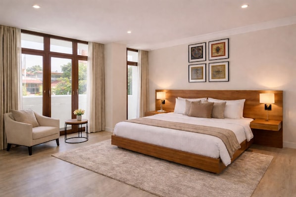 Un dormitorio amplio con una cama grande, una zona de estar con una silla y una mesa, y vistas a través de amplios ventanales.
