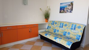 A small room with a sofa, orange cabinets, a potted plant, and a wall-mounted picture. - Appart. Air conditioning, beach access, 6 people, terrace, private parking CAP D'AGDE Rochelongue (Cap d'Agde)